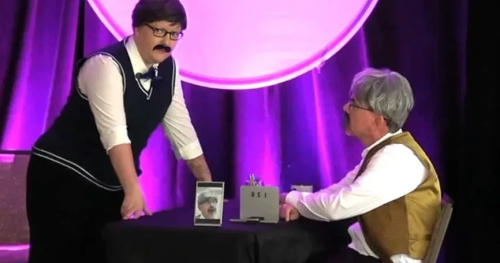 Jason and Kristin on stage with wigs and false moustaches have a corporate discussion