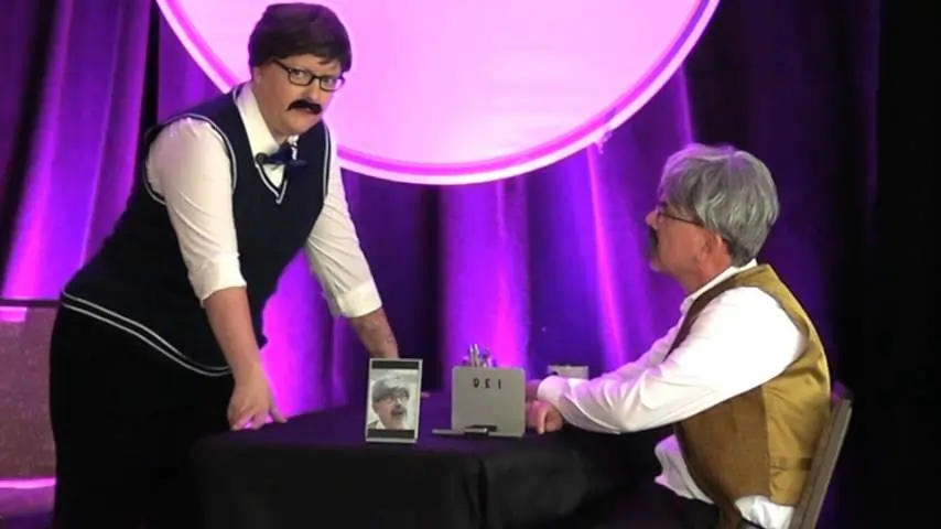 Jason and Kristin on stage with wigs and false moustaches have a corporate discussion